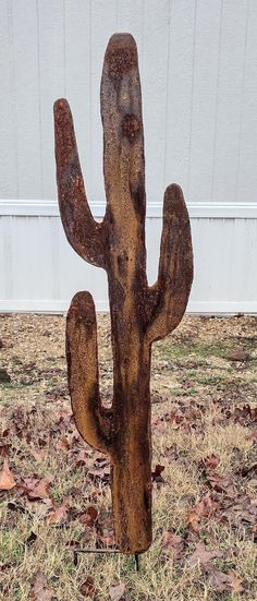 a metal cactus sitting on top of a dry grass field next to a white building