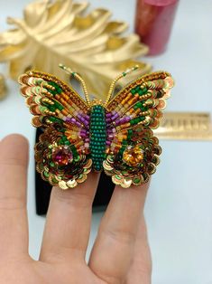 a hand holding a colorful butterfly brooch on it's finger with other items in the background