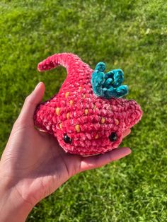 a hand holding a small crocheted toy in the grass