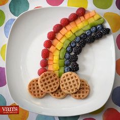 a white plate topped with waffles and fruit next to a rainbow shaped cookie