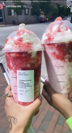 two people holding up cups with ice cream and strawberries in them on the street