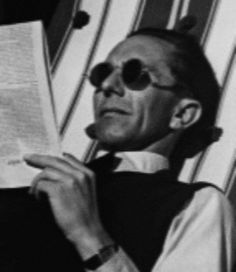 black and white photograph of a man in sunglasses reading a book while sitting on a beach chair