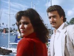 a man and woman standing next to each other in front of sailboats on the water