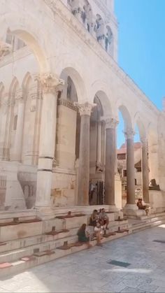 two people sitting on the steps in front of an old building with arches and pillars