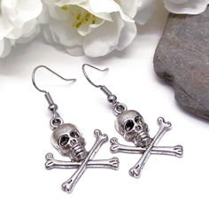 Dangly earrings with silver tone skull and bones charms. The earrings are ca 40mm (1.57 inches) long including hooks. Silver coloured hooks that comply with strict regulations for low nickel and lead content in jewellery. Bone Colored Metal Earrings For Pierced Ears, Nickel-free Skull Earrings In Punk Style, Silver Skull Earrings With Skull Print, Silver Skull Earrings With Ear Wire, Nickel Free Metal Skull Earrings, Metal Skull Earrings With Ear Wire, Skull-shaped Metal Earrings With Ear Wire, Skull Shaped Metal Earrings, Skull And Crossbones