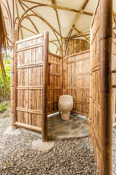 an outdoor toilet in a bamboo structure with rocks and gravel on the ground under it