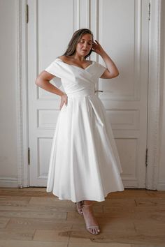 a woman in a white dress posing for the camera with her hands on her head