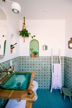 a bathroom with green tiles and blue flooring is pictured in this image, there are plants hanging on the wall