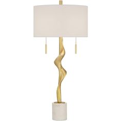 a gold and white table lamp with a white shade on the top, in front of a