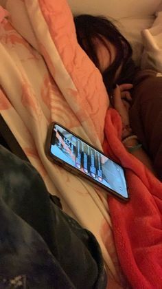 a person laying in bed with a cell phone on top of their head and blanket