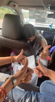 three people sitting in the back seat of a car with their hands on each other's thumb