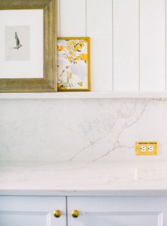 a kitchen counter with white cabinets and yellow knobs on the cabinet doors, in front of a framed painting