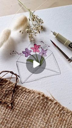 an envelope with flowers in it sitting on top of a piece of paper next to some pens