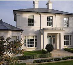 a large white house with lots of windows and bushes in front of the entrance to it