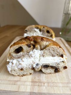 two pieces of bread with cream and raisins sitting on a wooden cutting board