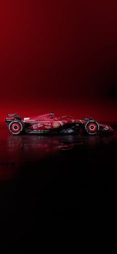 a red race car is shown on a black surface with a red light in the background