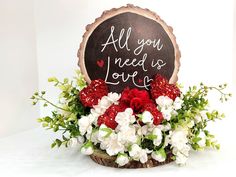 a wooden sign with flowers and greenery in it that says all you need is love