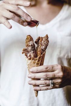 a woman is eating chicken and waffles from an ice cream cone with syrup