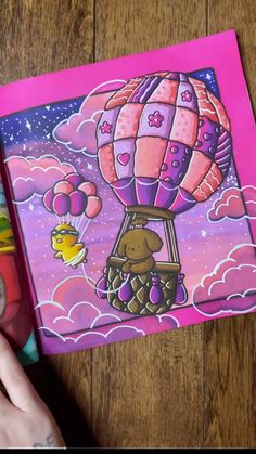 someone is holding up a pink book with an image of a hot air balloon in the sky