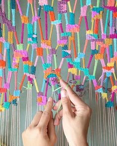 two hands are working on an art project made out of string and colorful yarns