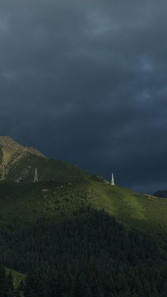 dark clouds loom over the top of a mountain with a white tower in the foreground