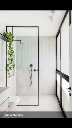 an all white bathroom with black accents and greenery on the shower wall, along with glass doors