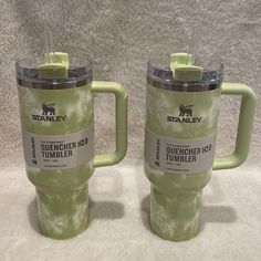 two green travel mugs sitting next to each other on top of a white blanket