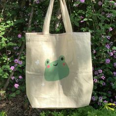 a bag with a frog on it hanging in front of some purple flowers and bushes