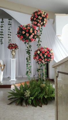 three tall white vases filled with pink and red flowers on top of a table