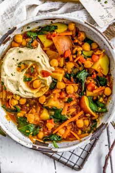 a white bowl filled with chickpeas, carrots and spinach topped with hummus