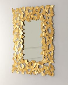 a mirror with gold leaves on it hanging on the wall next to a white wall