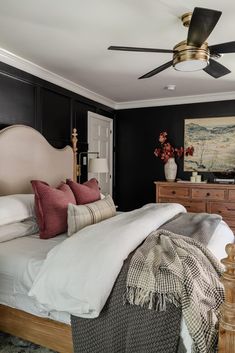 a bedroom with black walls, white bedding and a ceiling fan in the corner