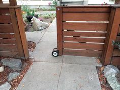 two wooden gates on the side of a sidewalk next to rocks and plants in front of a house