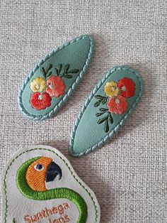 two embroidered patches with flowers on them sitting next to each other, one in the shape of a bird