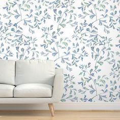 a white couch sitting in front of a blue and white wallpaper with leaves on it