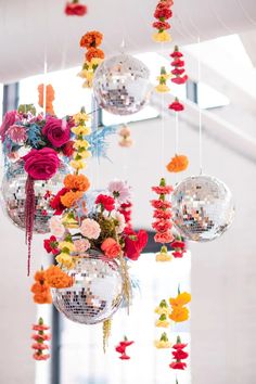 several disco balls hanging from the ceiling with flowers in them and decorations attached to it