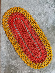 a crocheted doily with red and yellow trim on a gray surface next to a pair of scissors