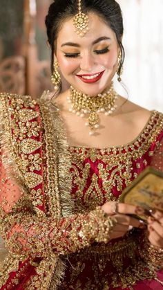 a woman in a red and gold bridal outfit smiles while holding a small box