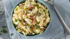 a blue bowl filled with pasta salad next to a silver spoon and fork on top of a napkin