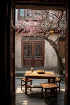 an open door with a table and bench in front of a pink blossoming tree