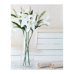 white flowers are in a clear vase on a table next to rolled up papers and a roll of paper