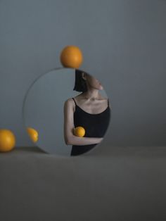 a woman standing in front of a mirror with oranges flying around her