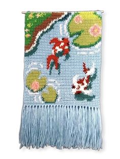 a cross stitched wall hanging with fish and lily pads on blue yarn, featuring goldfish