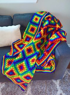 a colorful crocheted afghan sits on a gray couch next to a white pillow