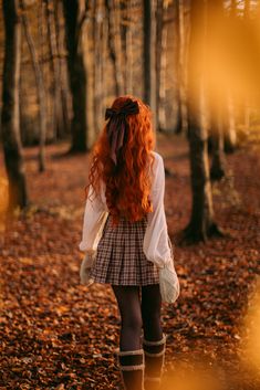 a woman with red hair is walking through the woods