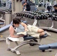 a man laying on top of a bench next to a gym equipment rack with dumbbells in the background