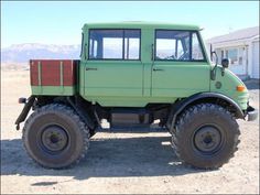 a green truck parked on top of a dirt field