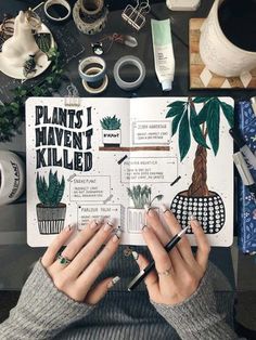 a person holding a notebook with plants and other things on the table behind them,