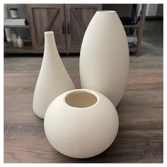 three white vases sitting on top of a wooden table next to each other in front of a cabinet