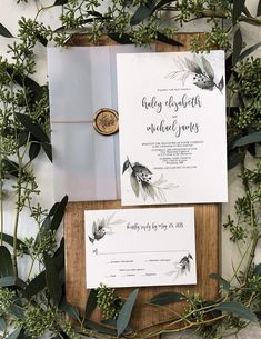 the wedding stationery is surrounded by greenery and eucalyptus leaves, including an envelope with a wax stamp